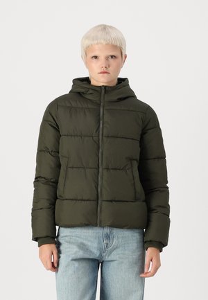 Olijfgroene pufferjack met een capuchon, ritsluiting en gewatteerde textuur. Voorzien van zijzakken en stevige manchetten. Draag over lichtblauwe jeans.