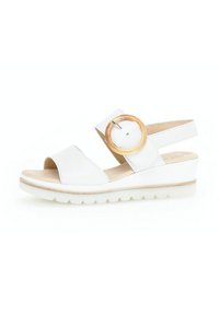 Sandalias de cuña blancas con un acabado de piel suave, con punta abierta y una cinta ancha. Detalle notable de acento de madera redonda en la correa ajustable.