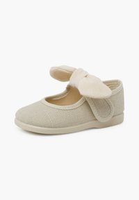 Zapato de lona beige claro con un upper texturizado, suela flexible y un lazo de tela a juego en la correa. Estilo Mary Jane.