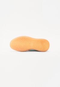 Suela de zapato con patrones circulares texturizados en goma de color naranja claro. La parte superior presenta un material suave de color aqua.
