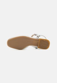 Sandalia de cuero plateado con puntera redonda, correa ajustable en el tobillo y suela de goma con el nombre de la marca "paul green" estampado.