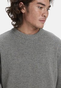 Grau gestrickter Pullover mit geripptem Rundhalsausschnitt und subtiler gesprenkelter Struktur. Enganliegendes Design, hergestellt aus weichen, gemischten Materialien.