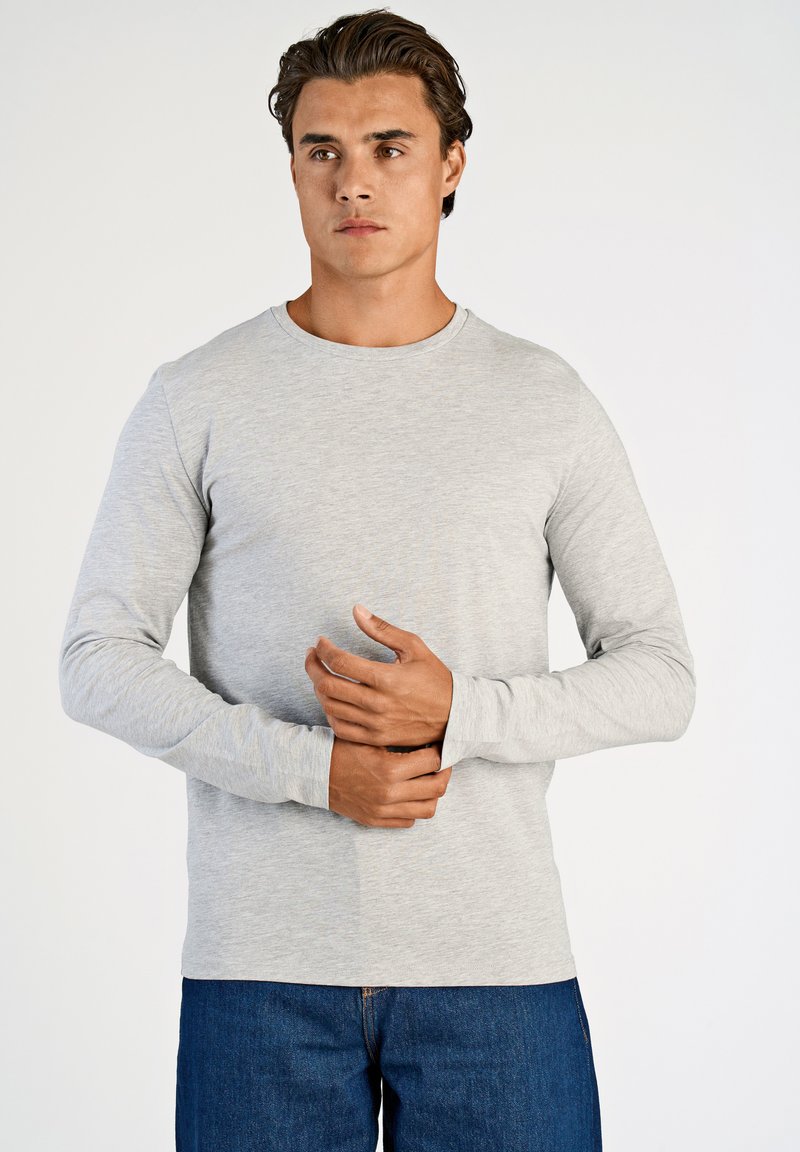 Harmaa pitkähihainen t-paita, jossa on pyöreä kaula-aukko ja joka on valmistettu pehmeästä materiaalista. Paita on istuvat hihat ja se on yhdistetty sinisiin farkkuihin.