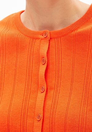 Close-up van een persoon die een feloranje geribbelde cardigan draagt met vijf zichtbare geopende knopen aan de voorkant.