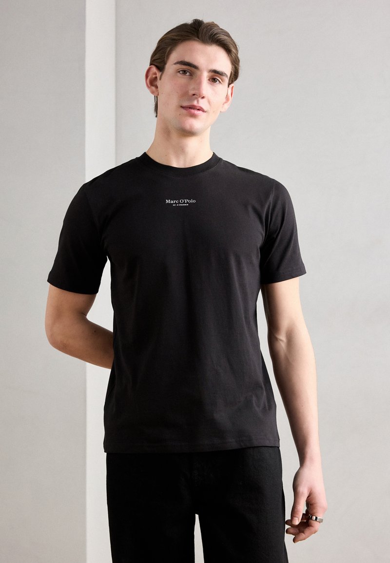 Tricou negru din bumbac, cu mâneci scurte, decolteu rotund și logo alb "Marc O'Polo" pe piept. Purtați cu pantaloni închiși la culoare, textură netedă.