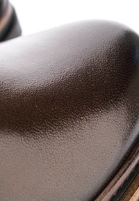 Gros plan sur l’avant d’une chaussure en cuir marron foncé texturé avec des coutures visibles le long du bord de la semelle et une forme lisse et arrondie.