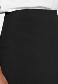 Jupe noire ajustée avec une texture lisse, présentant une coupe structurée, des poches cachées et un design de couture épuré.