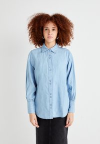 Lys blå denimskjorte med knappestolpe foran, klassisk krage og lange ermer med samlede mansjetter. Glatt tekstur og uformell design.
