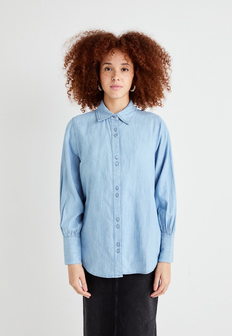 Lys blå denimskjorte med knappestolpe foran, klassisk krage og lange ermer med samlede mansjetter. Glatt tekstur og uformell design.