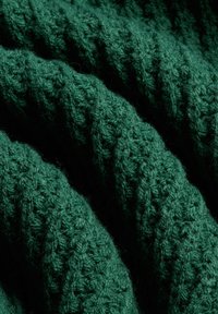 Nahaufnahme von dunkelgrünem Strickstoff, der eine detaillierte gewebte Textur und weiche, dicke Garnschlaufen zeigt.