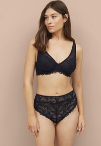 Schwarzes Spitzen-Bralette mit floralem Muster und gewellten Kanten, kombiniert mit passendem hochgeschnittenem Spitzen-Höschen, beide mit weichen Texturen.