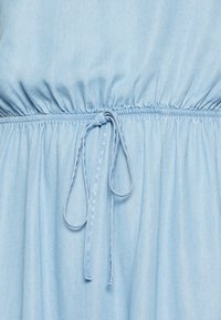 Světle modré šaty se sklady, elastickým pasem a detailem na zavazování. Měkká tkanina s kombinací bavlny a jemnou strukturou.