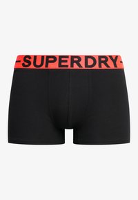 Schwarze Boxershorts mit einfarbigem Design, mit einem roten, elastischen Bund, auf dem "SUPERDRY" in schwarzen Buchstaben gedruckt ist.
