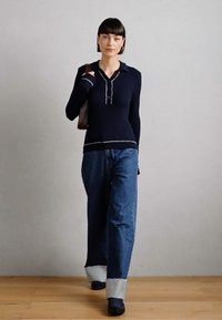 Top de punto acanalado de manga larga en color navy con un cuello y tres botones, combinado con jeans de denim sueltos con dobladillo y calzado oscuro.
