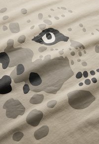 Beige stof med et stort abstrakt dyrehoveddesign med grå og sorte pletter. Bemærkelsesværdige detaljer inkluderer et fremtrædende øje og varierende teksturer.