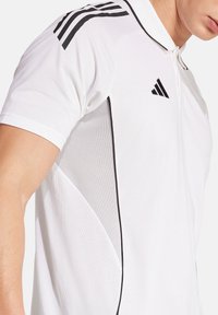 T-shirt polo bianco con accenti neri sulle spalle e sul colletto. Realizzato in un tessuto testurizzato con una vestibilità leggera e atletica.