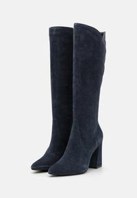 Bottes hauteur genou en daim bleu marine, avec bouts pointus et talons blocs, présentées côte à côte debout sur un fond blanc.