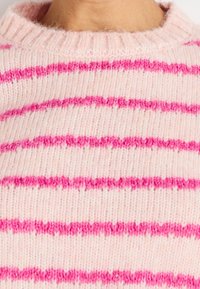 Zacht roze gebreide trui met heldere roze horizontale strepen, zichtbaar bij de halslijn en de bovenborst.