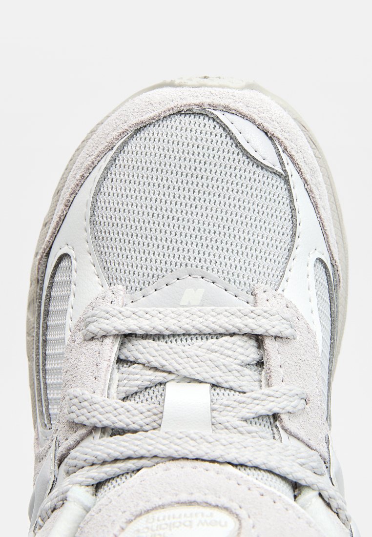 Zapatillas grises con parte superior de malla, acentos de gamuza, cordones planos y suela texturizada. El logo está sutilmente integrado en la lengüeta.