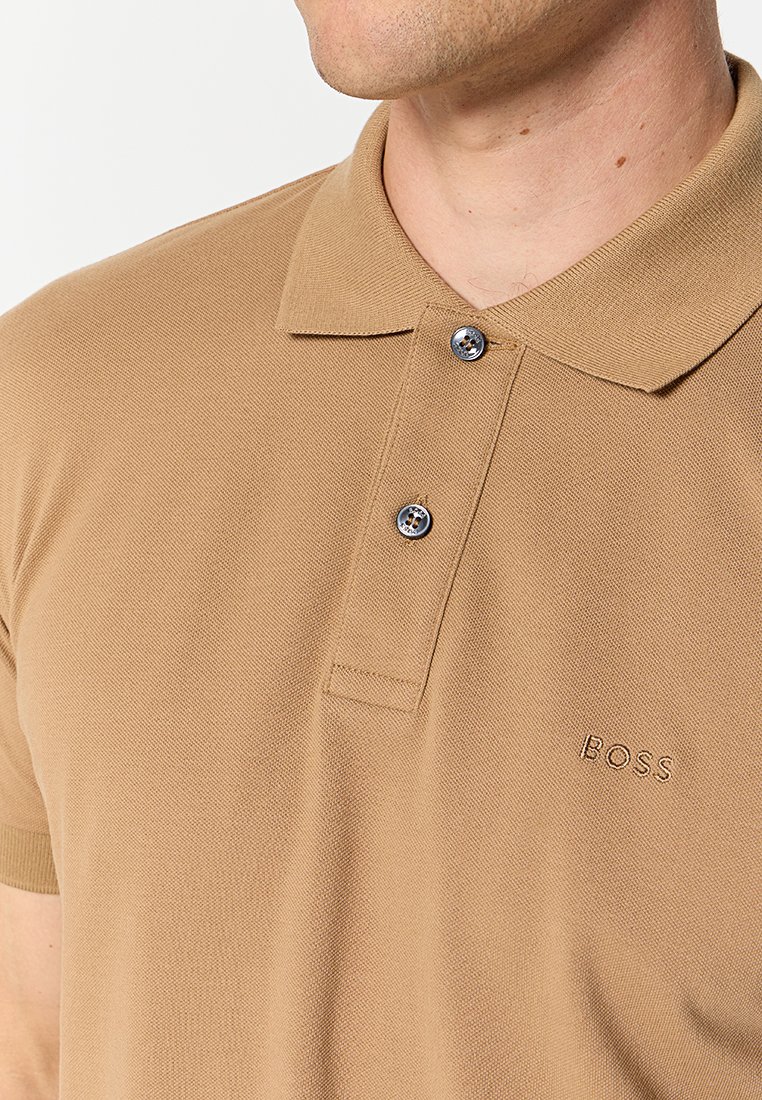 Polo shirt tan en tissu texturé avec un col, une patte de boutonnage à deux boutons et le logo "BOSS" brodé sur la poitrine gauche.