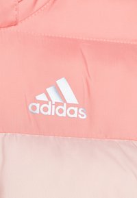 Roze stof met het witte Adidas-logo en drie diagonale strepen gestikt op een textieloppervlak.