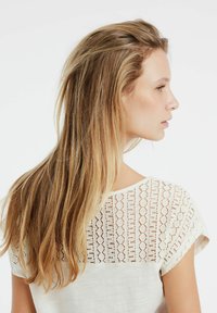 Witte blouse met een textuur van kant aan de achterkant met een geometrisch patroon. Zacht stof, korte mouwen en een relaxte pasvorm.