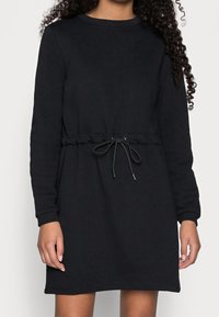 Svart sweatshirtklänning med långa ärmar, midja med dragsko, slät textur, rund halsringning och ribbade manschetter.