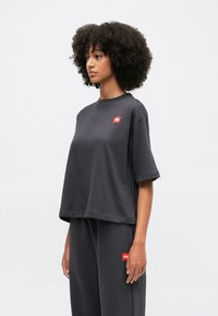 T-shirt nera cropped in cotone morbido con maniche corte, caratterizzata da un piccolo logo rosso sul petto. Abbinata a pantaloni neri coordinati.