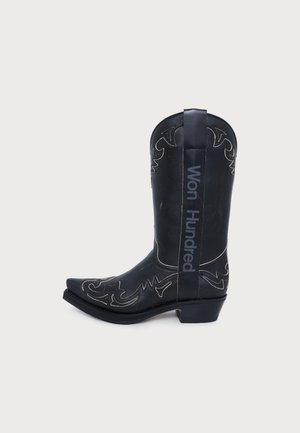 Botte de cowboy en cuir noir avec des surpiqûres décoratives, un bout pointu, un talon bas et une bride portant l’inscription « Won Hundred ».