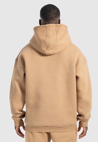 Sudadera beige de gran tamaño con una gran capucha, puños acanalados y dobladillo, con una textura de tela suave y un diseño trasero sin costuras.