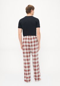 Schwarzes Kurzarm-T-Shirt, kombiniert mit locker sitzenden Karopijama in Weiß, Rot und Grün. Der Stoff wirkt glatt und hat eine lockere Passform.