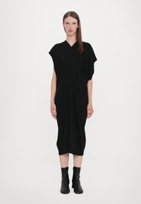 Black knee-length dress with a V-neck, batwing sleeves, and draped design. Made of soft fabric, paired with black ankle boots.