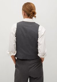 Szara kamizelka z tkaniny o dopasowanym kroju, zestawiona z białą koszulą. Kamizelka ma gładką fakturę i minimalistyczne detale, zaprojektowana dla eleganckiego wyglądu.