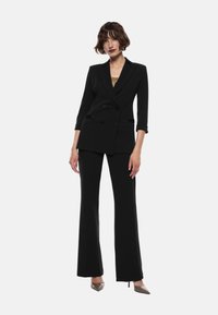 Blazer doppiopetto nero su misura con maniche a tre quarti abbinato a pantaloni a gamba larga. Tessuto morbido e design aderente.