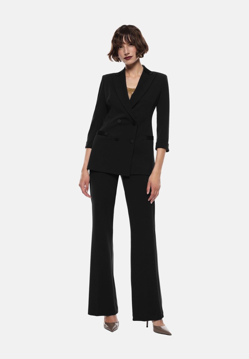 Blazer doppiopetto nero su misura con maniche a tre quarti abbinato a pantaloni a gamba larga. Tessuto morbido e design aderente.