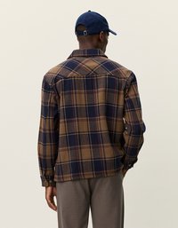 Brązowa i granatowa koszula flanelowa w kratę z długimi rękawami, mankietami na guziki i wyprofilowanym kołnierzykiem. Posiada prosty krój i wyprofilowaną część tylną.