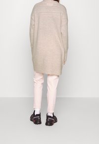 Maglione beige oversize con collo rotondo, abbinato a pantaloni rosa chiaro. Sneakers nere con suola testurizzata e accenti sottili.