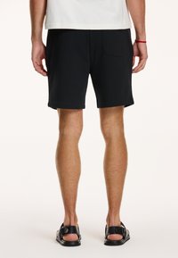 Schwarze Shorts aus einem Baumwollmix, mit lockerer Passform, Seitentaschen und einem schlichten Saum. Tragen Sie dazu schwarze Sandalen.