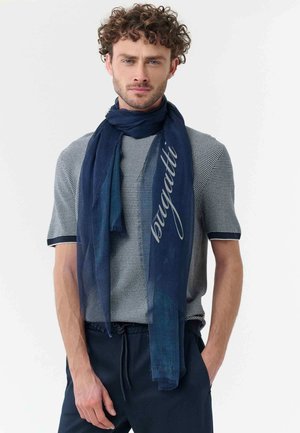 Man wearing a textured short-sleeve sweater and navy scarf with "Borgatti" text, standing with one hand in pocket against white background.