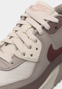 Κοντινή λήψη μπεζ και καφέ αθλητικού παπουτσιού Nike που δείχνει υφή δέρματος, υφάσματος πλέγματος, κορδόνια και το λογότυπο Nike swoosh στο πλάι.