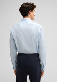Lichtblauwe shirt met lange mouwen en knoopmanchetten, gecombineerd met donkerblauwe broek met elastische tailleband en twee achterzakken.