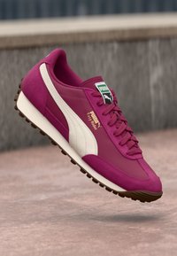 Puma Easy Rider tenisice imaju bordo gornji dio s kremastim akcentima, teksturirane slojeve i drvenu smeđu gumenu podlogu. Klasični dizajn s vezanjem.