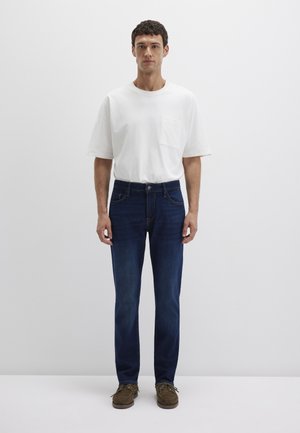 Herrenoutfit mit einem weißen Baumwoll-T-Shirt mit Brusttasche und dunkelb blauen Jeans. Strukturierter Stoff mit geradem Schnitt. Braune Schuhe.