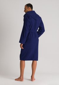 Accappatoio blu navy realizzato in morbido tessuto in spugna, dotato di cappuccio, maniche lunghe e una cintura abbinata, raggiungendo la lunghezza fino a metà polpaccio.