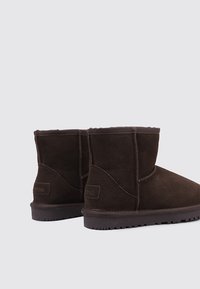 Botines de ante marrón con punta redondeada, forro suave y suela texturizada. Presentan una marca mínima en el lateral.