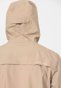 Beige vandtæt jakke med hætte, med teksten "W-PRO 10000" på den øverste del af ryggen og en ventilationsklap under skuldrene.