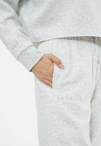 Hellgrauer cropped Sweatshirt und passende Jogginghose, aus strukturiertem Stoff, mit elastischem Bund und dezentem Logo-Detail am Bein.