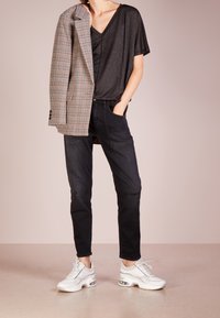 Černý top s výstřihem do V, blazer s houndstooth vzorem, černé džíny a bílé tenisky s průhlednou podrážkou. Blazer ležérně přehozený přes rameno.