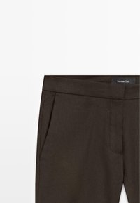 Pantaloni sartoriali marrone scuro con tasche laterali e fascia in vita, con etichetta Massimo Dutti all'interno.