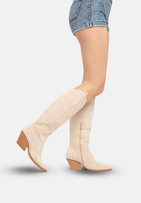 Knielange Cowboy-Stiefel aus beigem Veloursleder mit spitzer Zehe, dekorativer Naht und einem moderaten Blockabsatz. Reißverschluss an der Seite zum Verschließen.